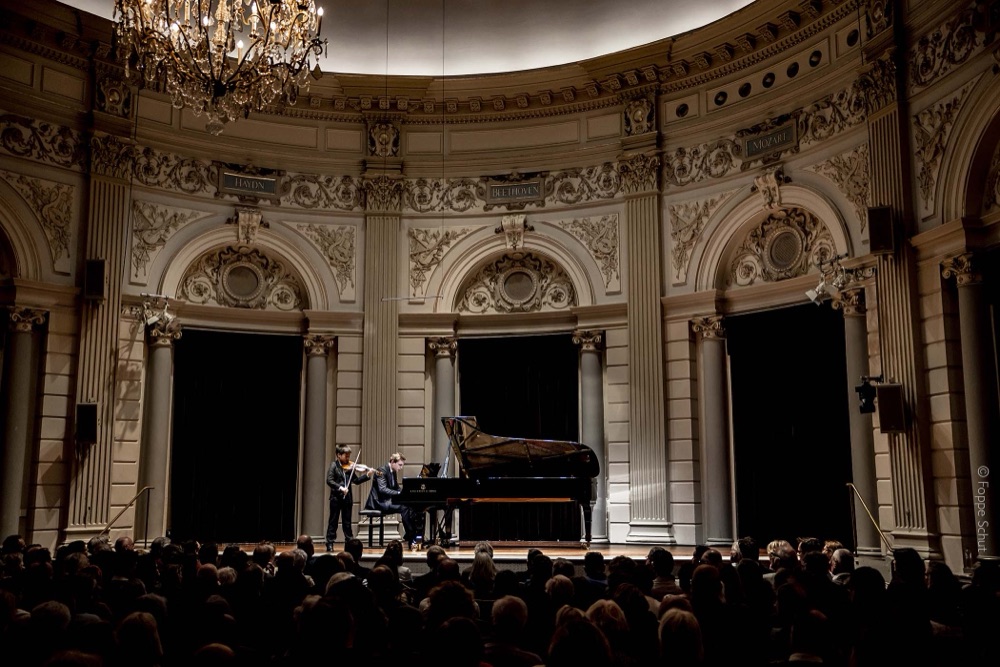 Student performing violin and piano duo in a concert hall